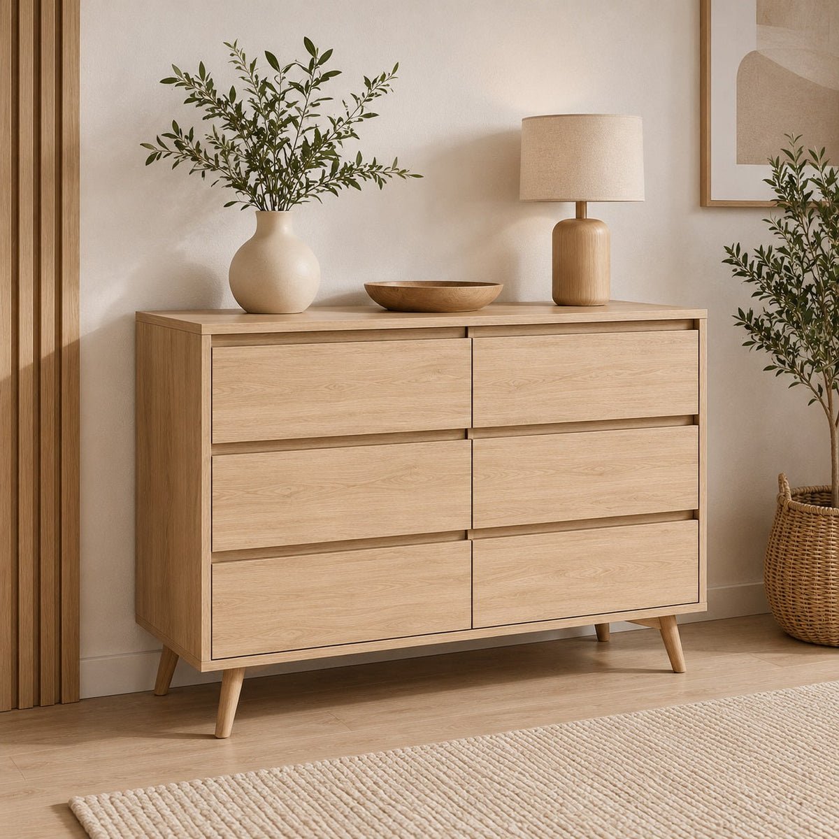 Commode scandinave en bois clair à 6 tiroirs sur pieds inclinés dans une chambre aux tons naturels.