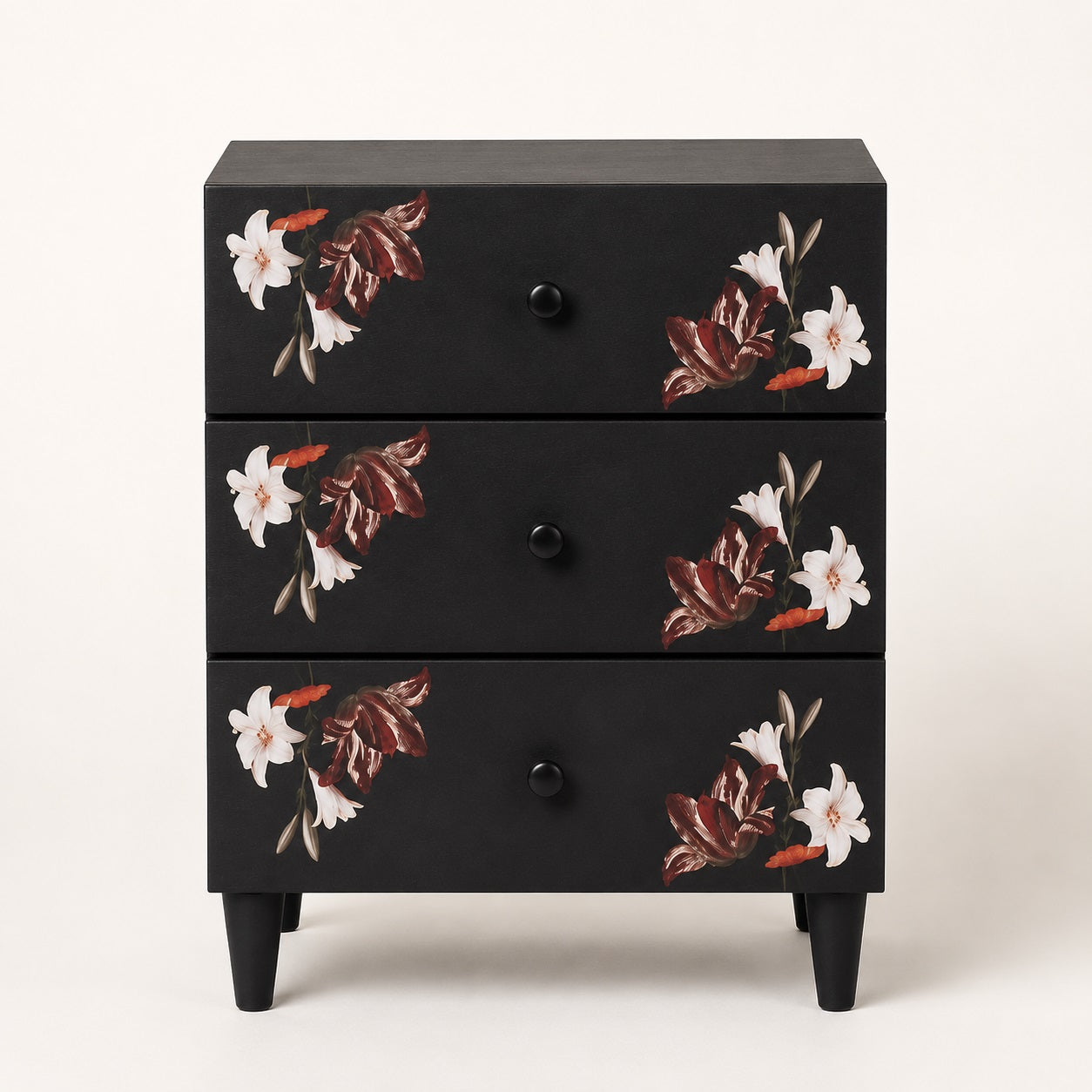 Vue de face d'une table de chevet noire design à trois tiroirs ornés de motifs floraux élégants.