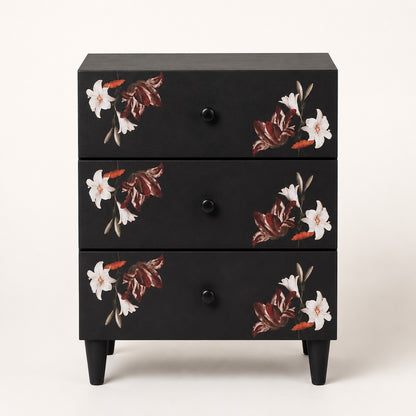 Vue de face d'une table de chevet noire design à trois tiroirs ornés de motifs floraux élégants.
