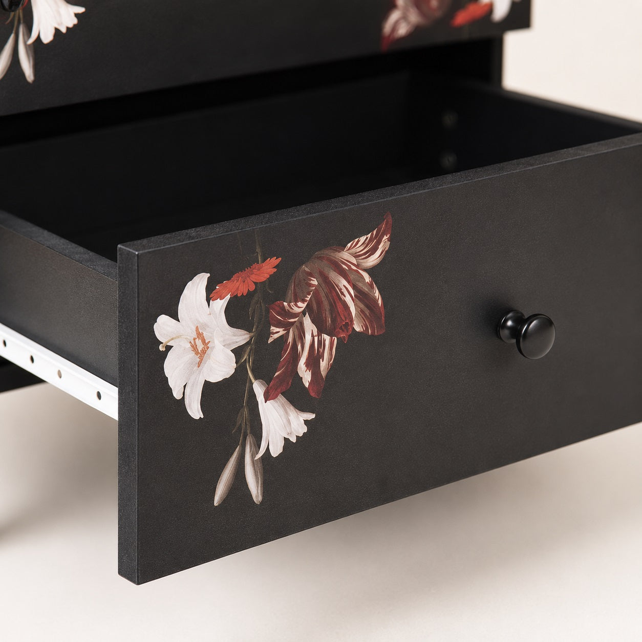 Gros plan sur un tiroir d'une table de chevet noire design avec motif floral et ouverture fluide.