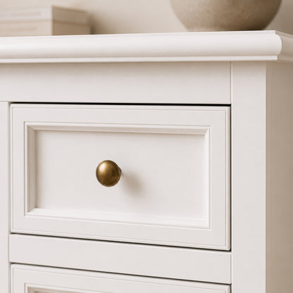 Détail d’un tiroir de commode vintage blanche avec façade moulurée et bouton rond finition dorée.