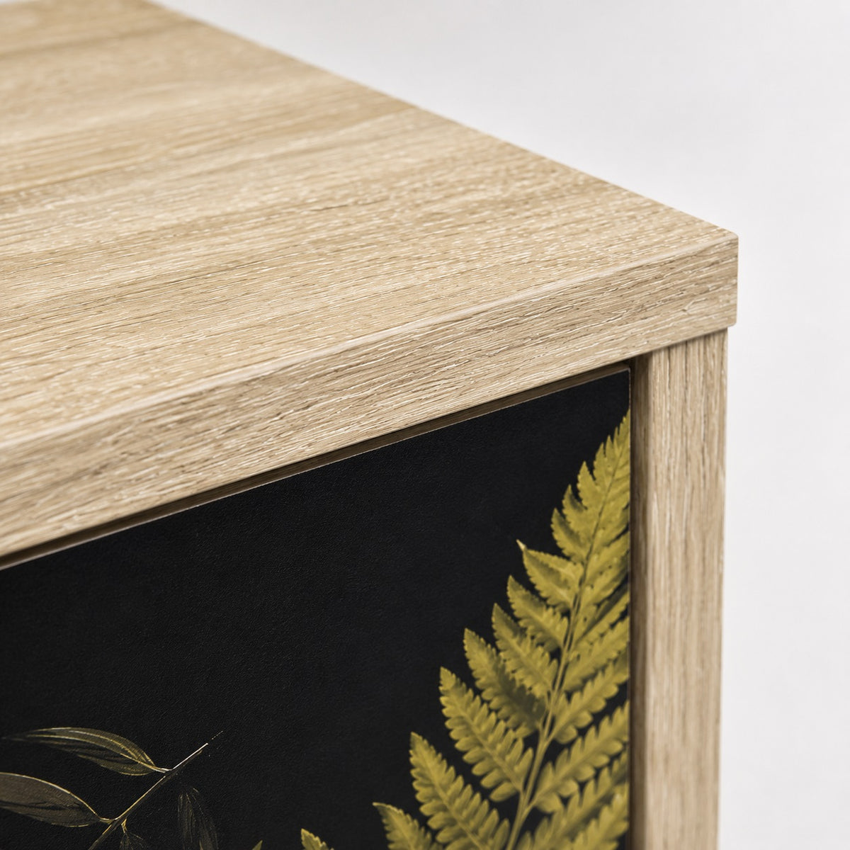 Zoom sur la finition bois clair de la commode 3 tiroirs Celia, commode design aux façades végétales noires.