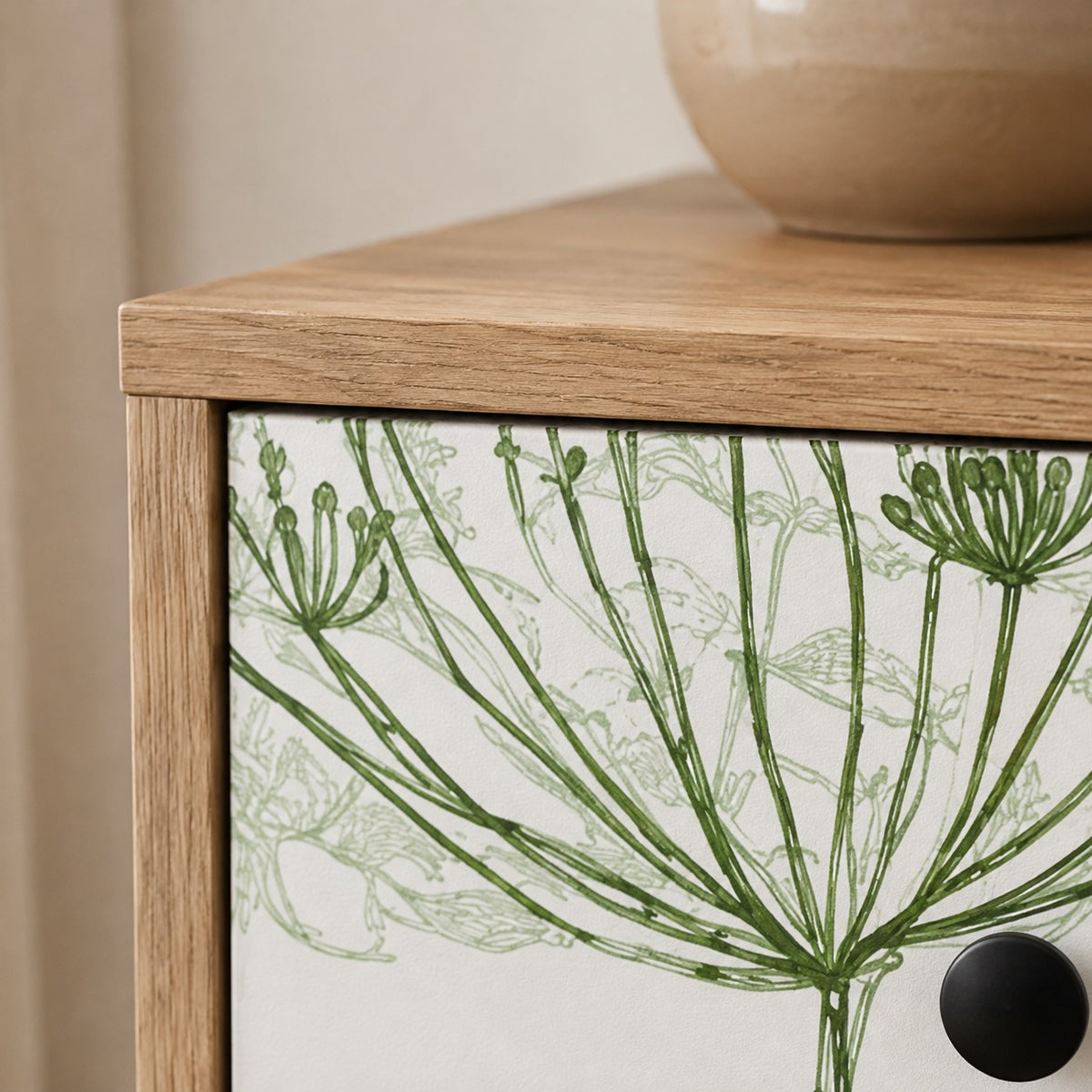 Détail de la commode design Dalia avec finition bois clair, motif végétal vert et poignée noire.