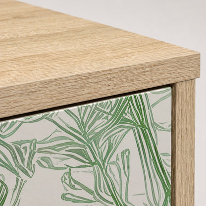 Détail de la commode design Dalia avec plateau effet bois clair et façade aux motifs végétaux verts.