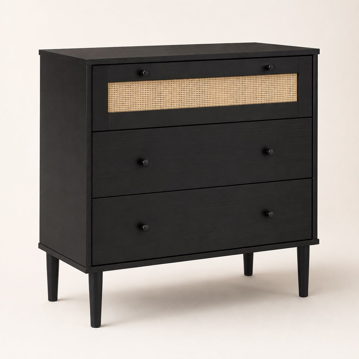 Commode 3 tiroirs noire avec façade en rotin naturel, poignées noires et pieds surélevés.