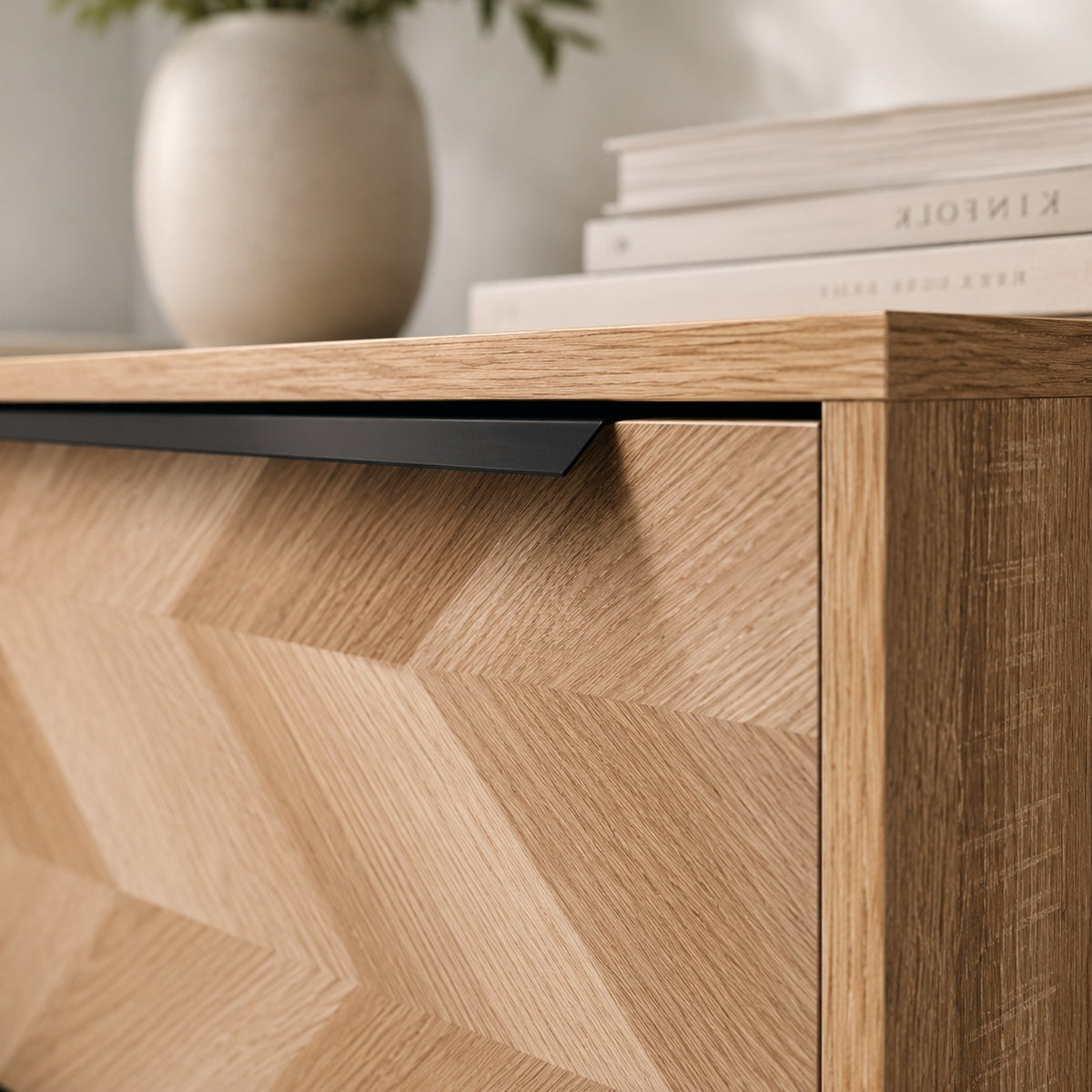 Détail de commode design en bois clair avec façade graphique et longue poignée noire contemporaine.