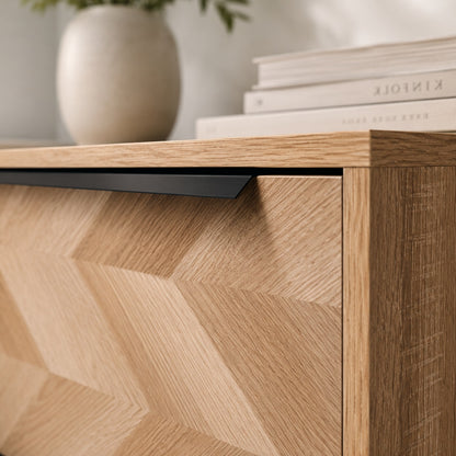 Détail de commode design en bois clair avec façade graphique et longue poignée noire contemporaine.