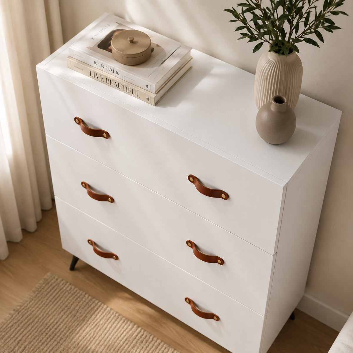 Vue en plongée de la commode 6 tiroirs blanche avec poignées effet cuir et plateau décoré.
