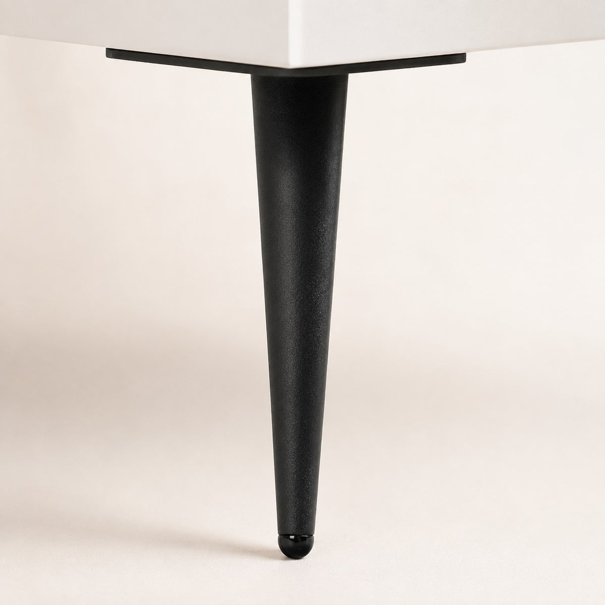 Détail du pied noir incliné de la commode 6 tiroirs blanche, pour un style moderne et épuré.