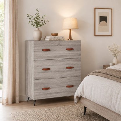 Commode 3 tiroirs grise Sylva vue de face, avec poignées effet cuir et piètement noir au design moderne.