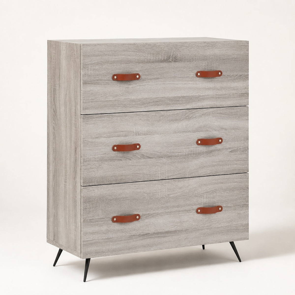 Commode 3 tiroirs grise Sylva, finition effet bois clair, poignées effet cuir et pieds noirs inclinés.